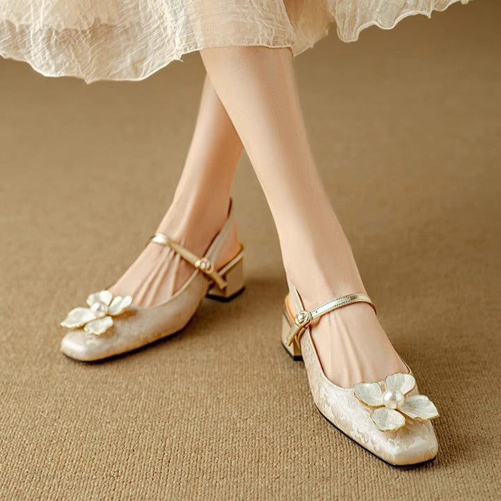 Woman wearing floral embellished pumps on a plain background.