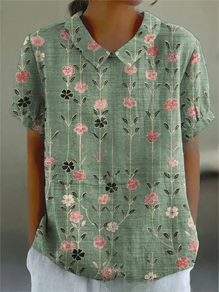 Female model wearing a floral blouse on a plain background.