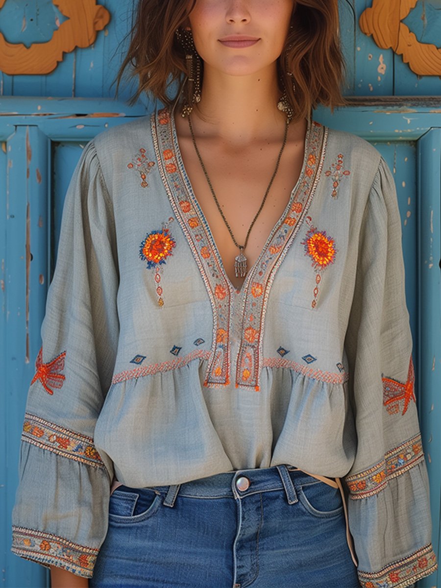 Woman wearing a bohemian embroidered V-neck blouse on a plain background.