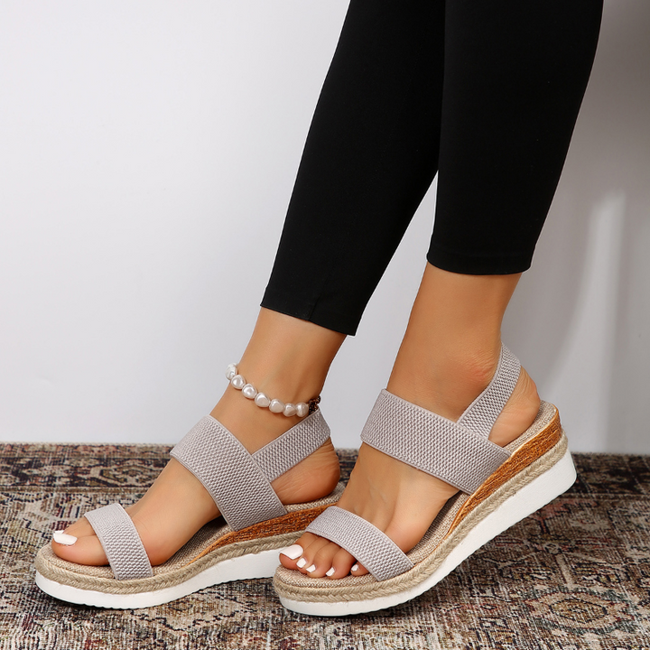 Female model displaying strappy cushioned sandals on a plain background with simple warm-weather style.