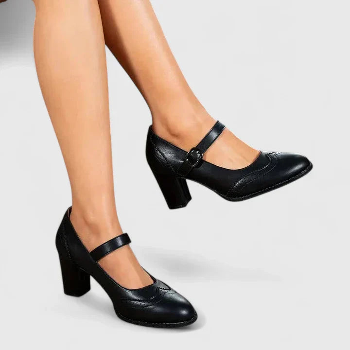 Female wearing brown buckle strap shoes with a block heel on a plain background.