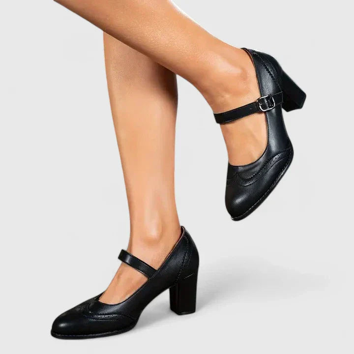 Female model wearing brown pointed toe strap heels on a plain background.