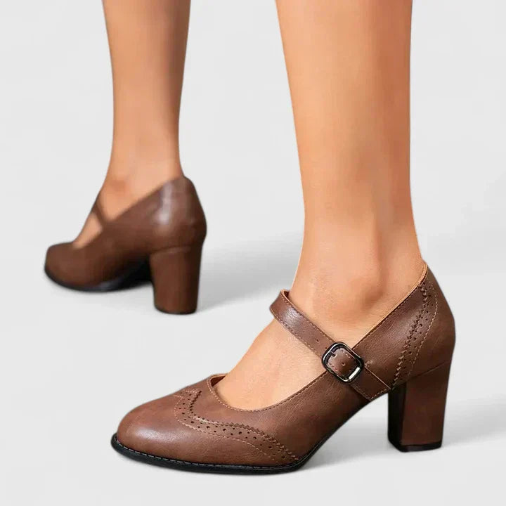 Female modelling brown strap block heel shoes on a plain background.