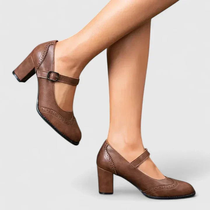 Woman standing in pointed toe Mary Jane heels against a plain background.