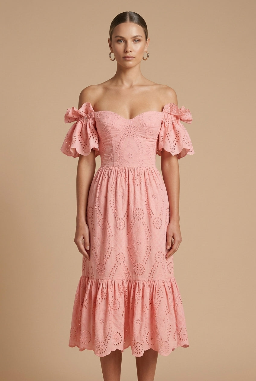 Female in a feminine eyelet midi dress with tiered skirt and bow sleeve accents on a plain background.
