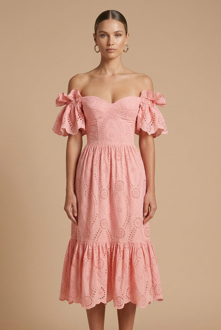 Female in a feminine eyelet midi dress with tiered skirt and bow sleeve accents on a plain background.