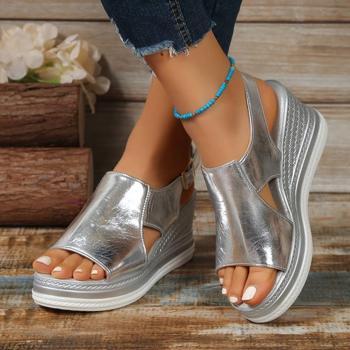 Woman wearing shimmering wedge sandals against a plain background.
