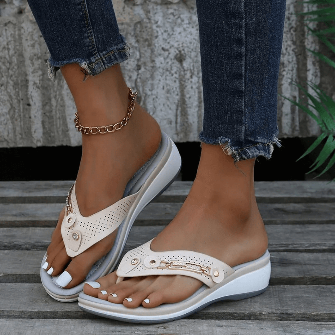 Woman modeling casual slip-on sandals with metallic details on a plain background.