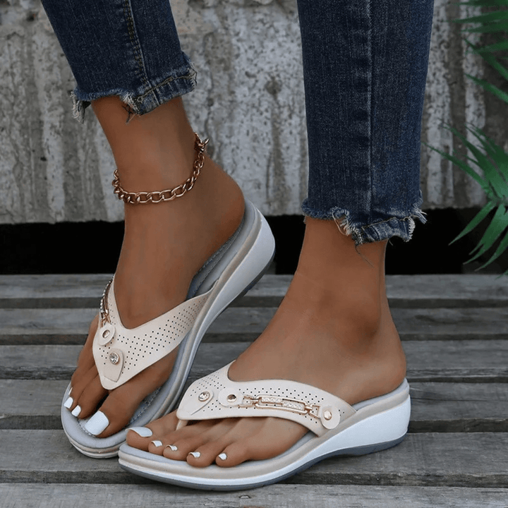 Woman modeling casual slip-on sandals with metallic details on a plain background.