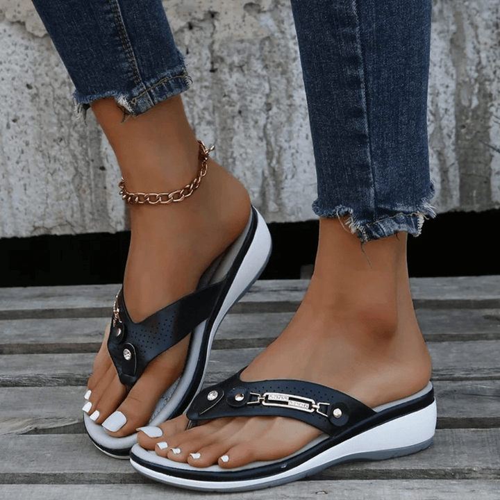 Female model wearing gold-accent summer sandals on a plain background.
