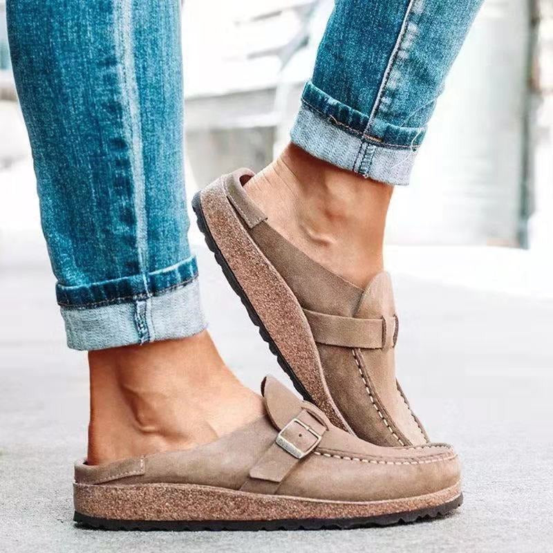 Female wearing slip-on loafers with buckle detail on a plain background.