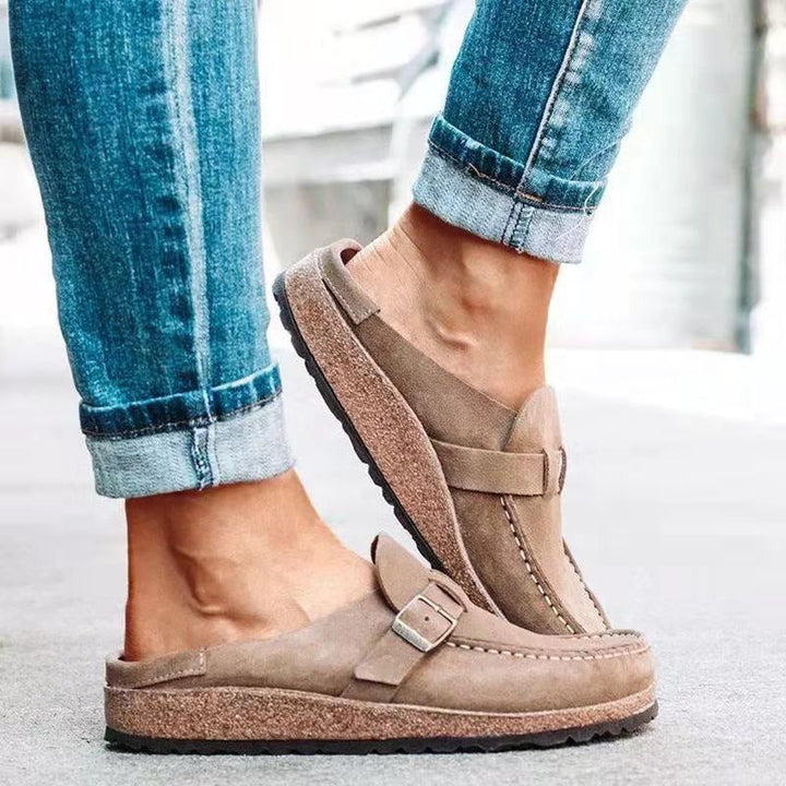 Female wearing slip-on loafers with buckle detail on a plain background.