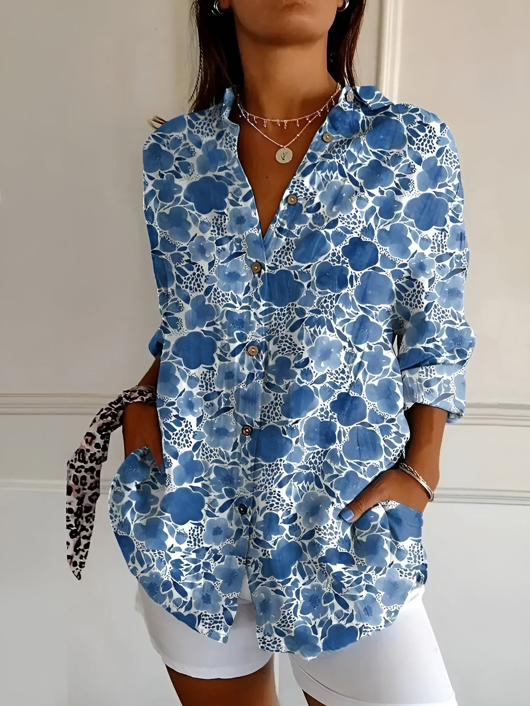 Female wearing a colorful floral button-front blouse on a plain background.
