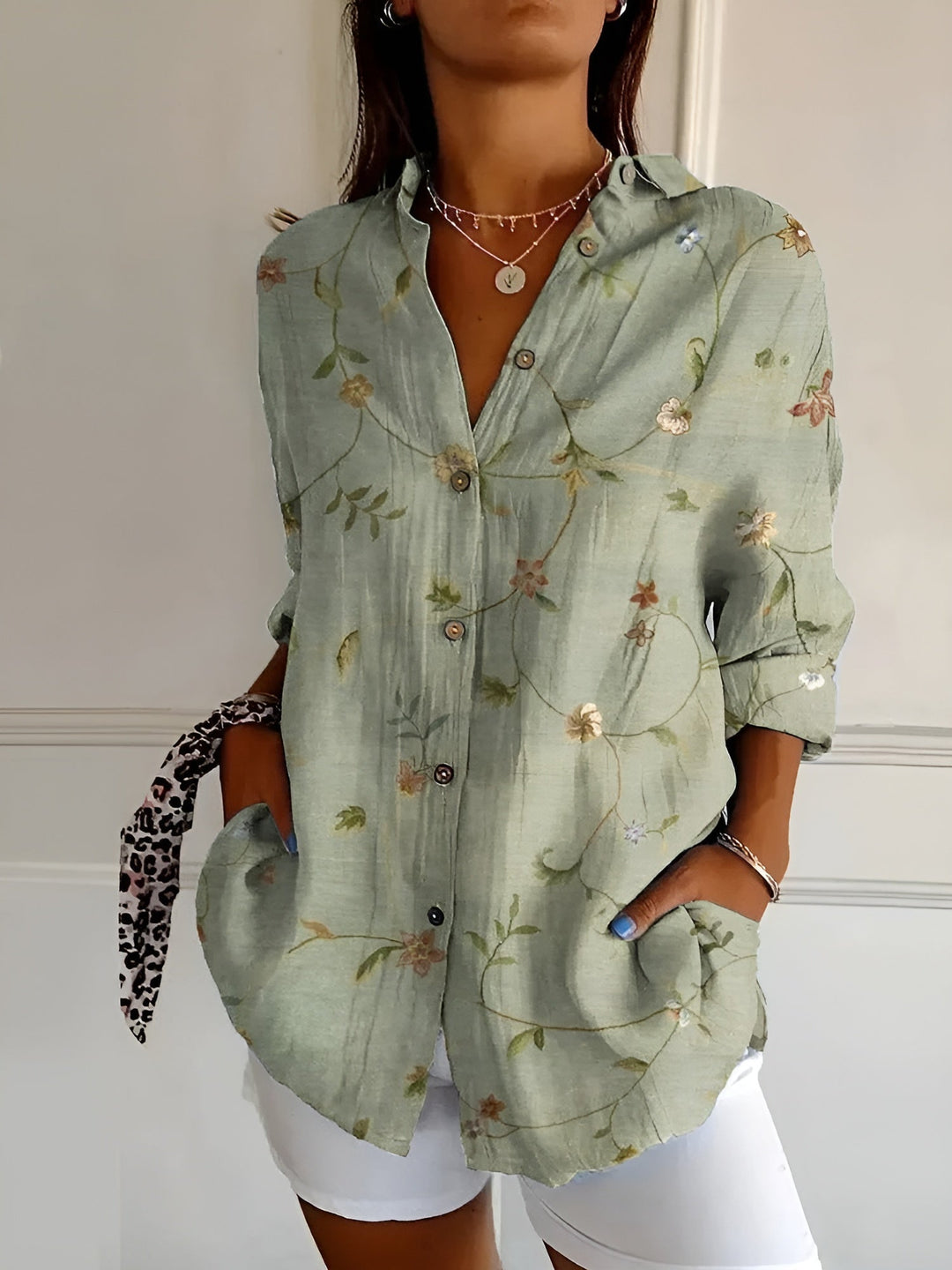 Woman in a loose floral summer blouse with short sleeves on a plain background.
