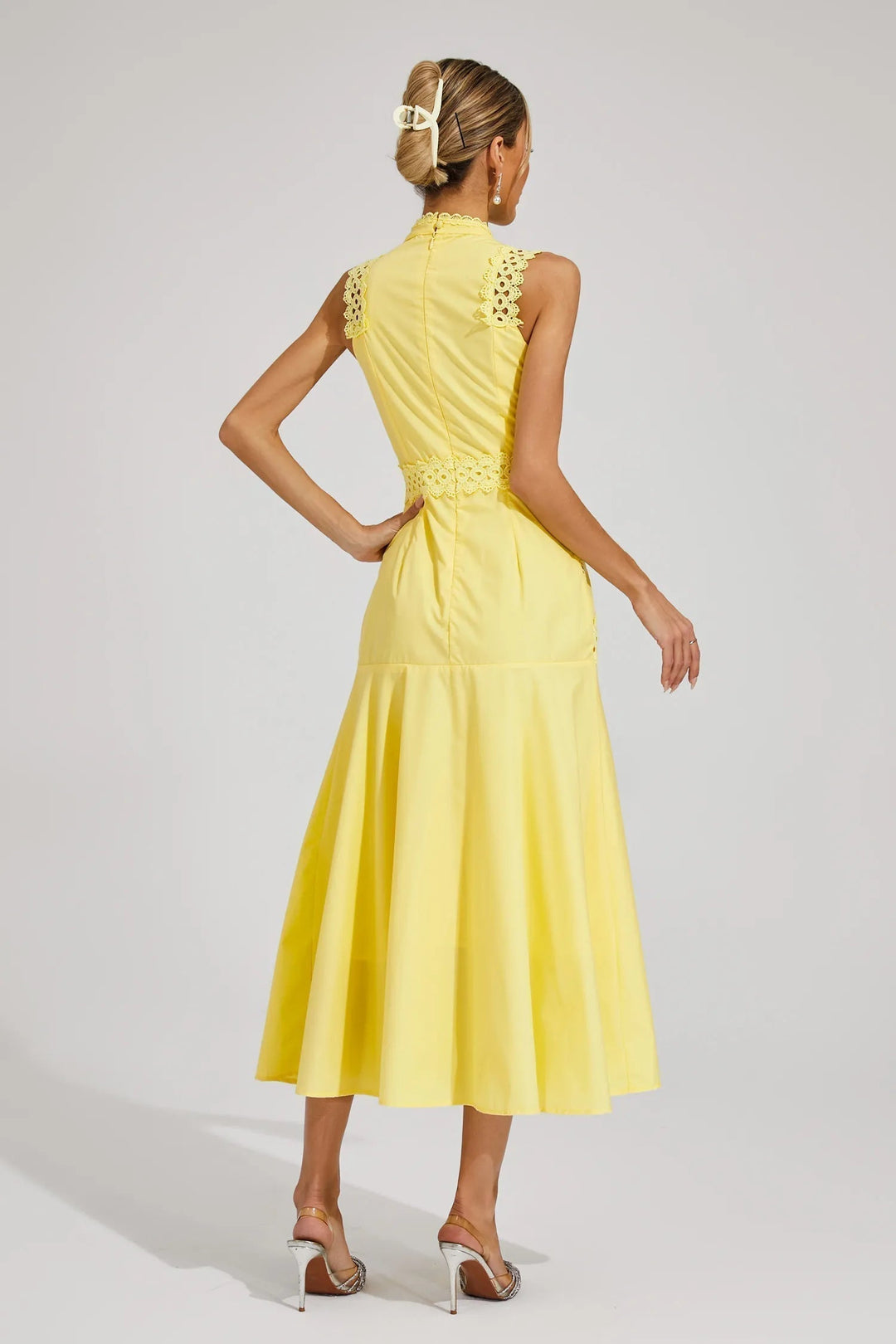 Woman styled in a sleeveless occasion dress with a softly shaped skirt on a plain background.