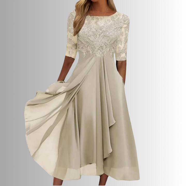 Woman showcasing an A-line midi dress with embroidered detail and side pockets against a plain background.
