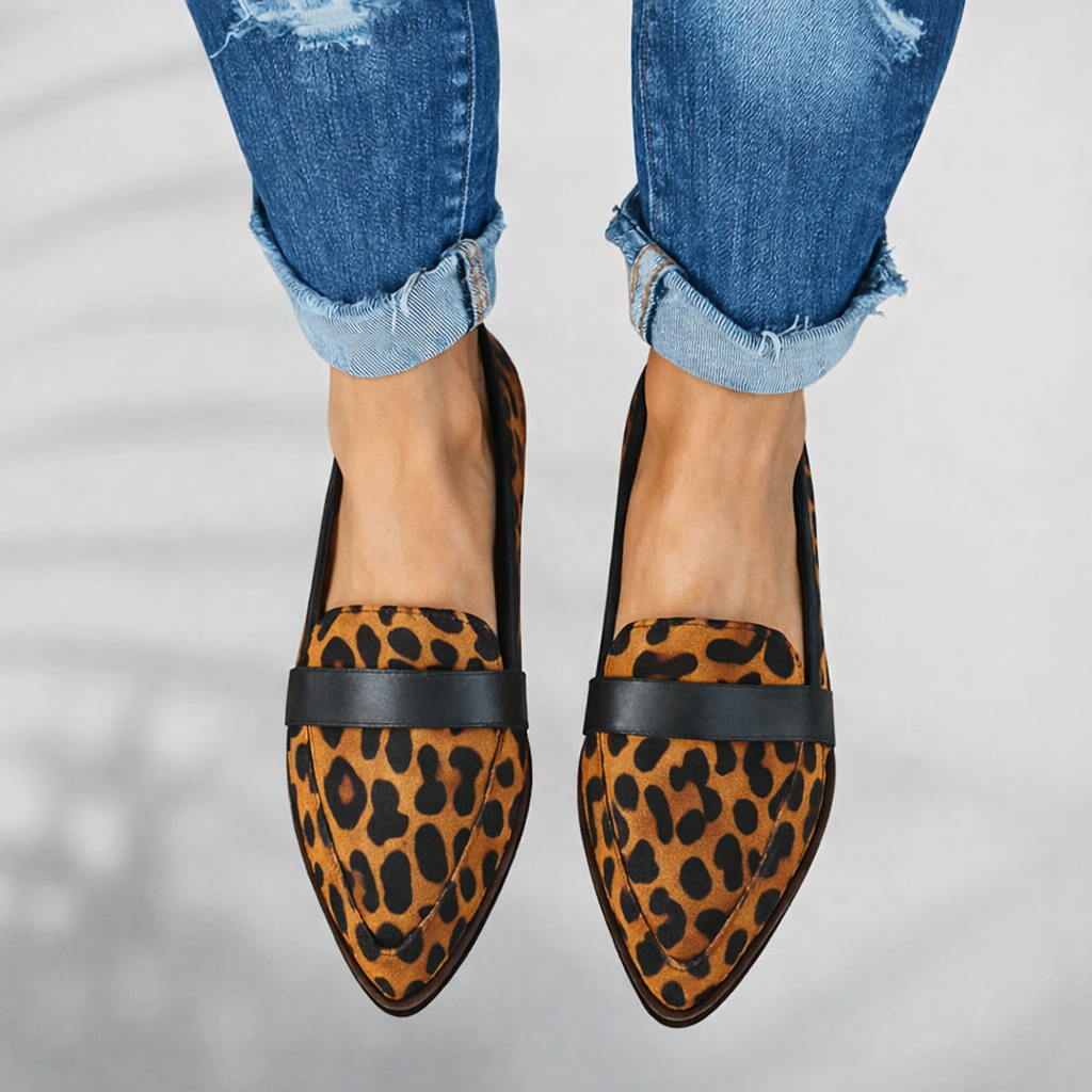Woman wearing polished pointed toe loafers on a plain studio background.