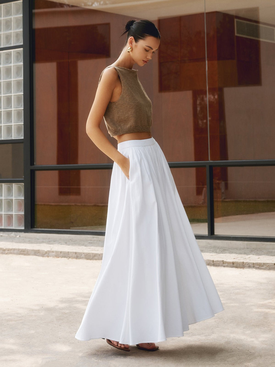 Woman wearing a high waist pleated A-line maxi skirt with pockets on a plain background.