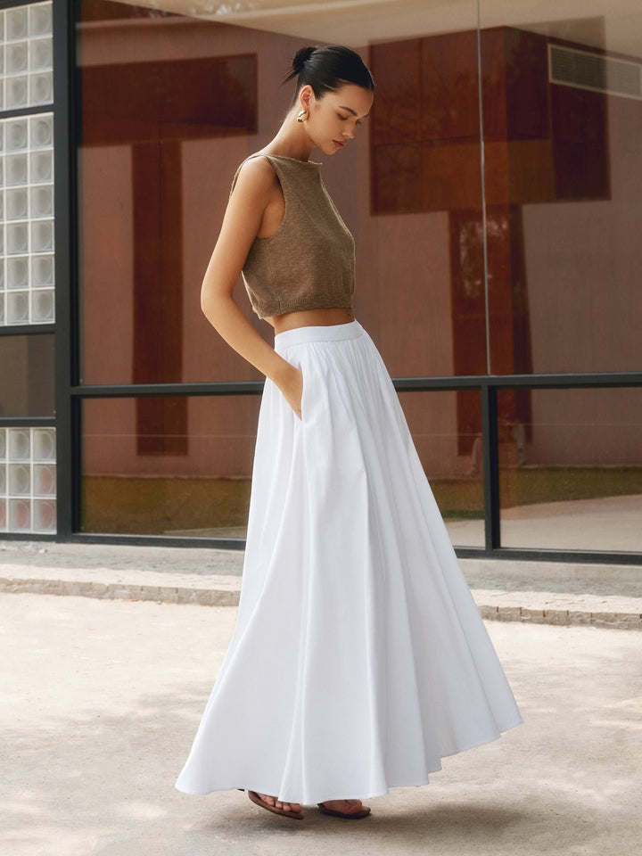 Woman wearing a high waist pleated A-line maxi skirt with pockets on a plain background.