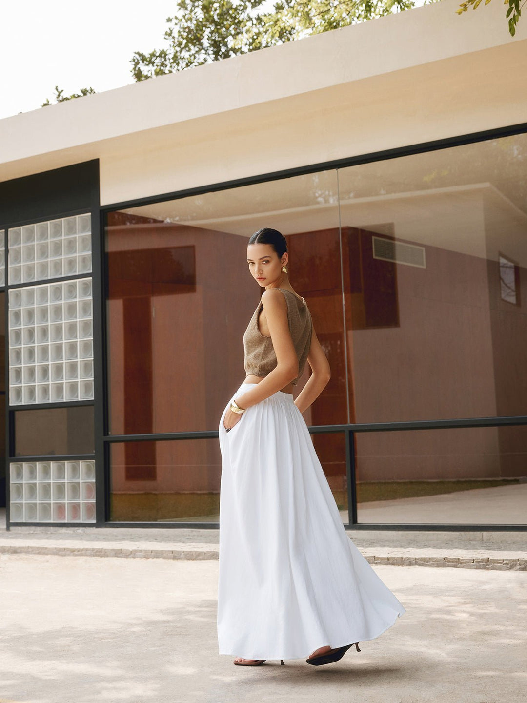 Woman styling a high waist A-line skirt with soft pleats on a plain background.