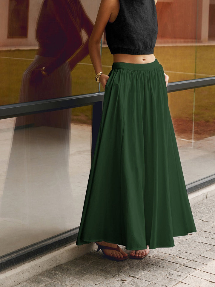 Woman wearing a pleated maxi skirt with a full-length hem on a plain background.