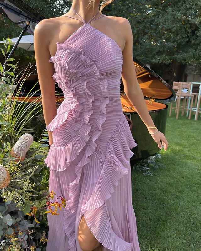 
Female displaying an occasion dress with draped details and an asymmetrical silhouette on a plain background.