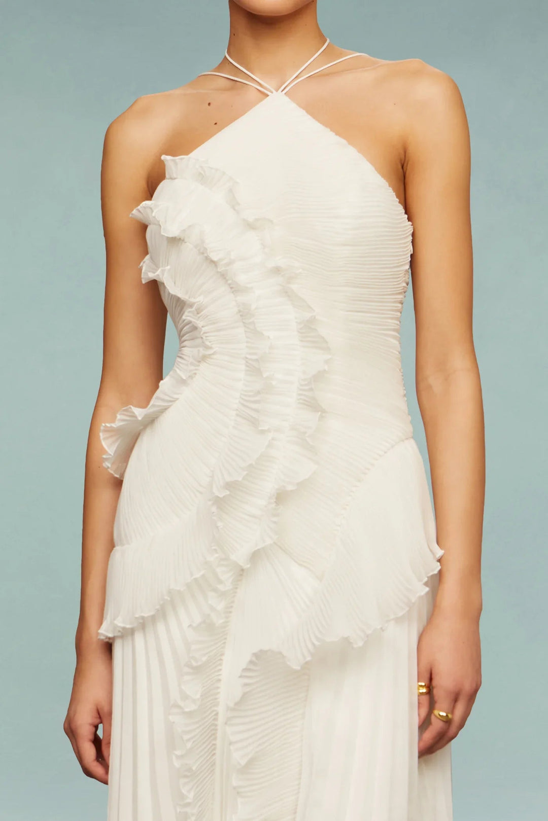 Woman in a one-shoulder maxi dress with elegant layered accents on a plain background.