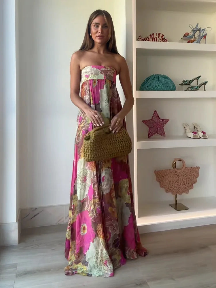  Woman showcasing a floral maxi dress with a strapless neckline and floor-length drape on a plain background.und