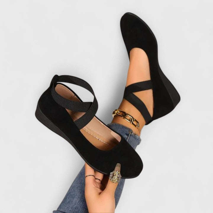 Woman wearing cross strap Mary Jane flats on a plain background.