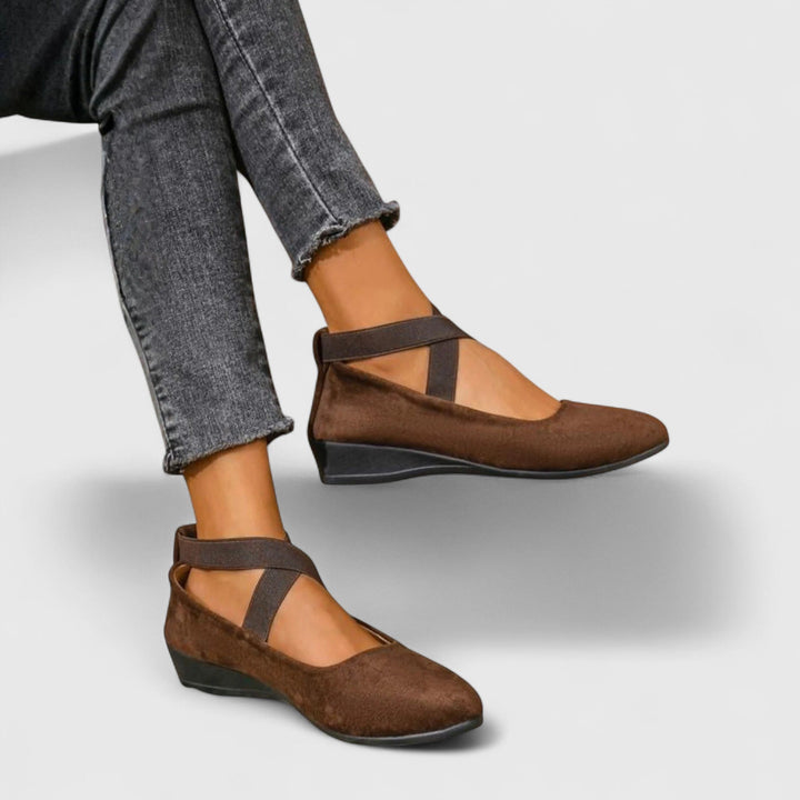 Woman modelling Mary Jane flats with wrap-around straps on a plain background.